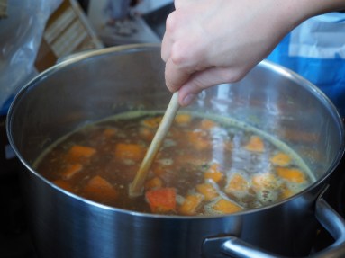 A wooden spoon stirring a pot of vegetables on the stove.